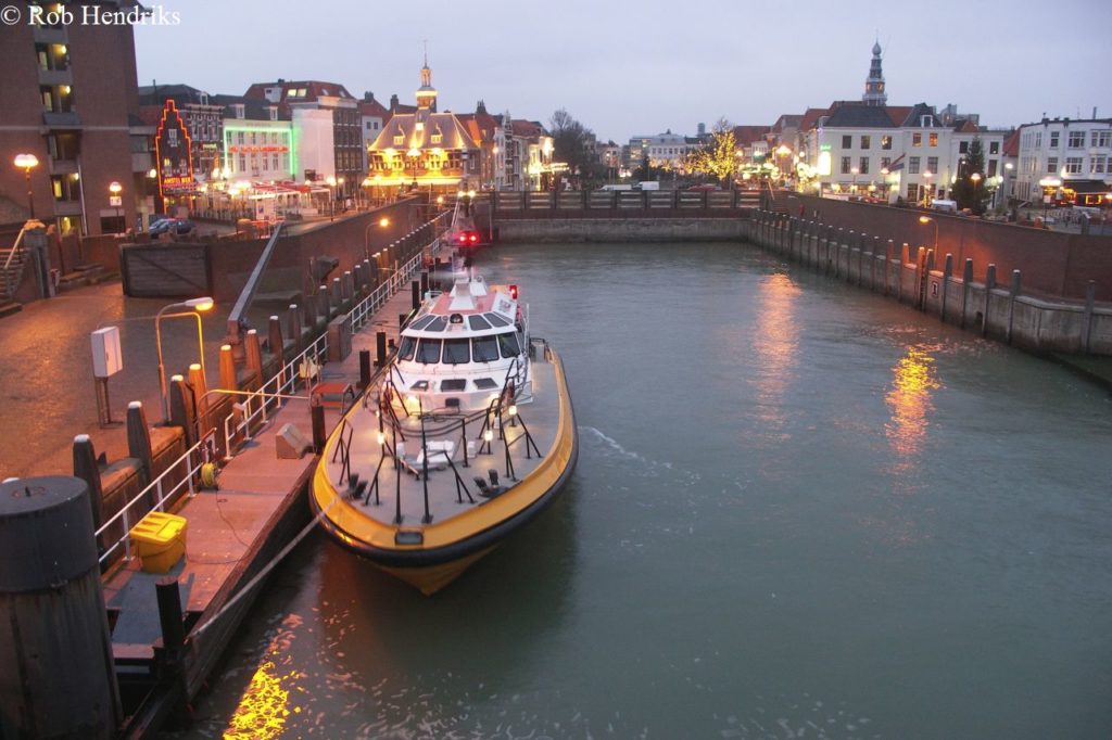 Loodsboot in de haven van Vlissingen bij avond met verlichte kade en historisch centrum tijdens stadswandeling